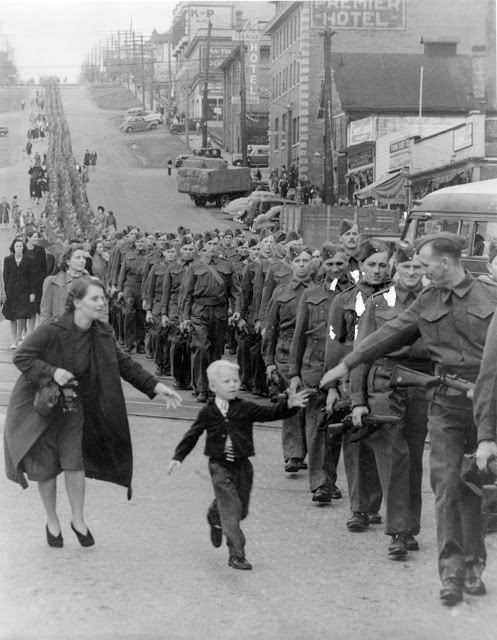"Wait For Me Daddy," by Claude P. Dettloff, October 1, 1940: A line of soldiers march in British Columbia on their way to a waiting train as five-year-old Whitey Bernard tugs away from his mother's hand to reach out for his father.